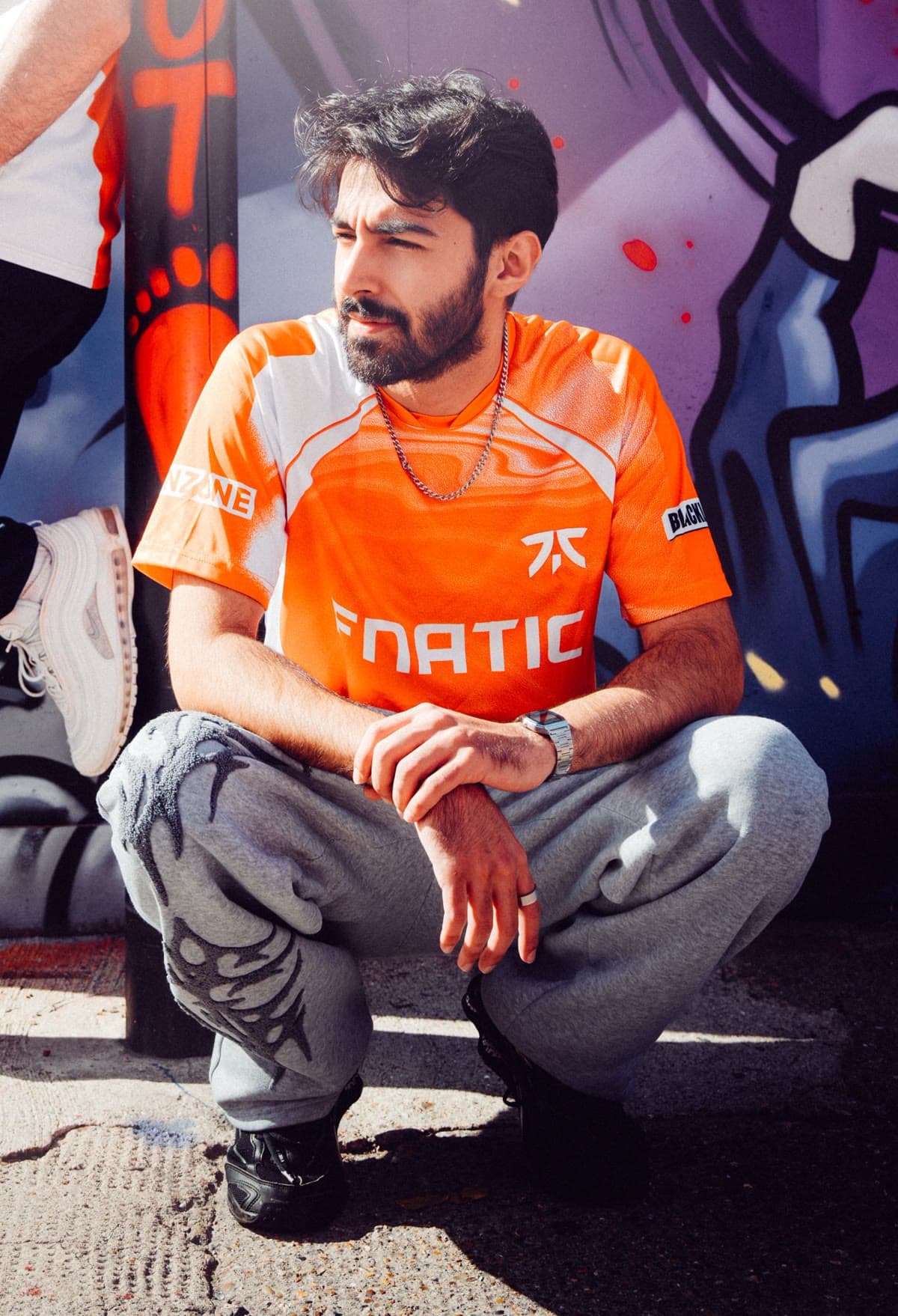 Isot crouched in front of a graffiti wall, wearing the orange Fnatic jersey